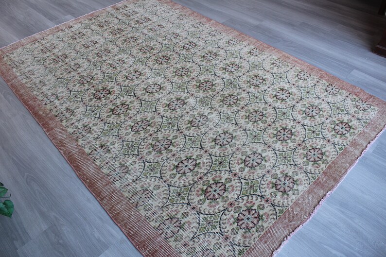 May include: A vintage rug with a cream background and a repeating pattern of pink, green, and black floral motifs. The rug has a pink border with frayed edges.