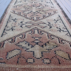 May include: A vintage rug with a geometric pattern in shades of beige, brown, and black. The rug has a worn and faded look, giving it a rustic and antique feel.