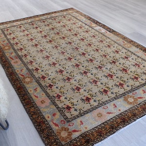 May include: A vintage rug with a floral pattern in shades of beige, brown, red, and blue. The rug has a border with a geometric design.