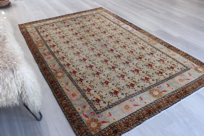 May include: A vintage rug with a floral pattern in shades of beige, brown, red, and blue. The rug has a border with a geometric design.