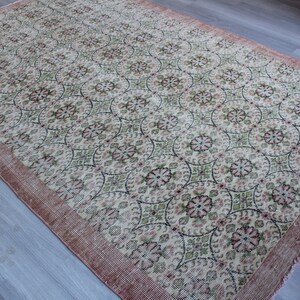 May include: A vintage rug with a cream background and a repeating pattern of pink and green floral motifs. The rug has a pink border.