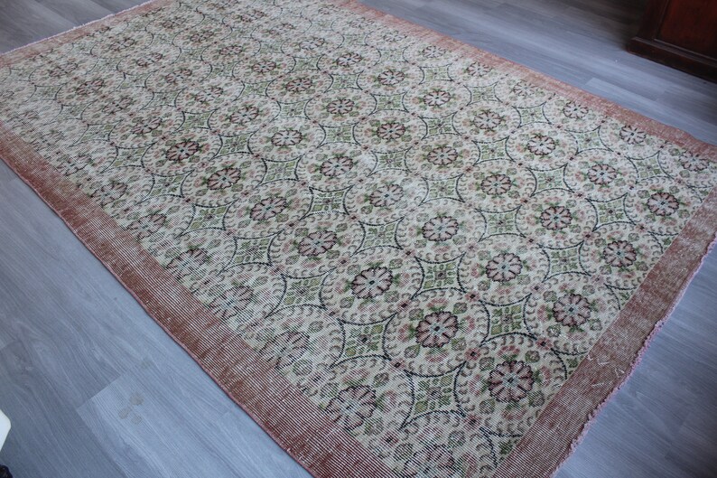May include: A vintage rug with a cream background and a repeating pattern of pink and green floral motifs. The rug has a pink border.