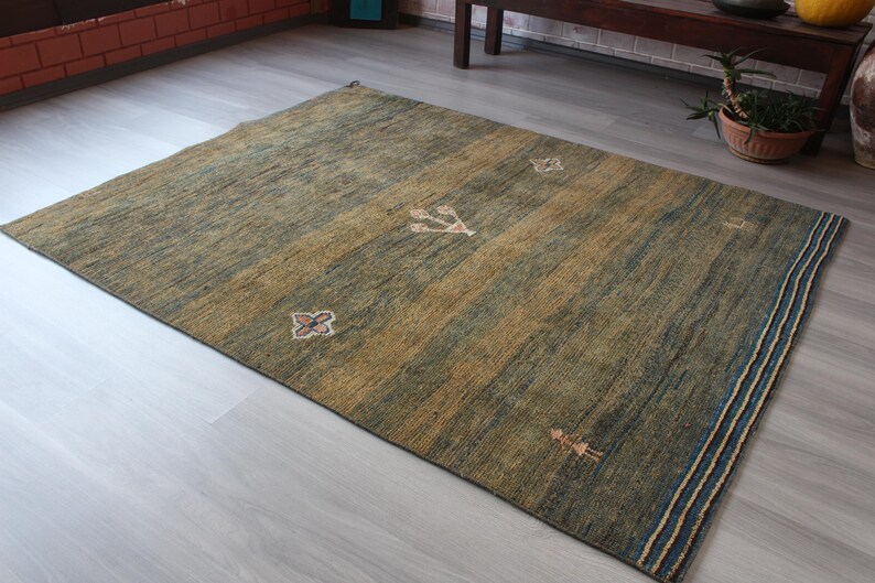 Op de afbeelding: Een groen en bruin vloerkleed met een geometrisch patroon. Het kleed heeft een blauwe en witte rand.