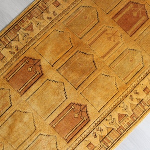 May include: A traditional Turkish prayer rug with a geometric pattern in shades of brown and gold. The rug has a fringed edge and is made of wool.