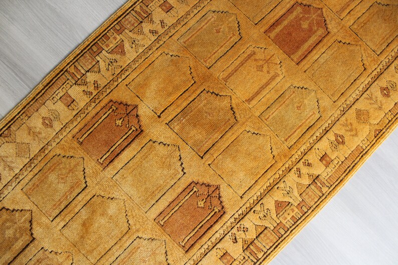 May include: A traditional Turkish prayer rug with a geometric pattern in shades of brown and gold. The rug has a fringed edge and is made of wool.
