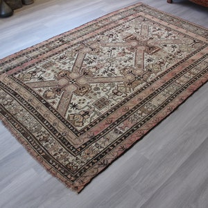 May include: A vintage rug with a cream background and intricate brown and pink geometric patterns. The rug has a faded, worn look, adding to its antique charm.