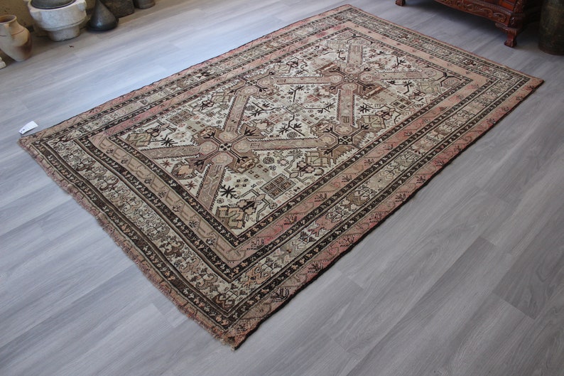 May include: A vintage rug with a cream background and intricate brown and pink geometric patterns. The rug has a faded, worn look, adding to its antique charm.