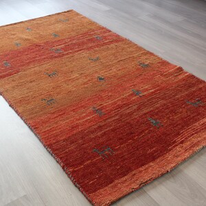 May include: A hand-woven rug with a gradient of orange, red, and brown hues. The rug features a subtle pattern of small, repeating shapes throughout.