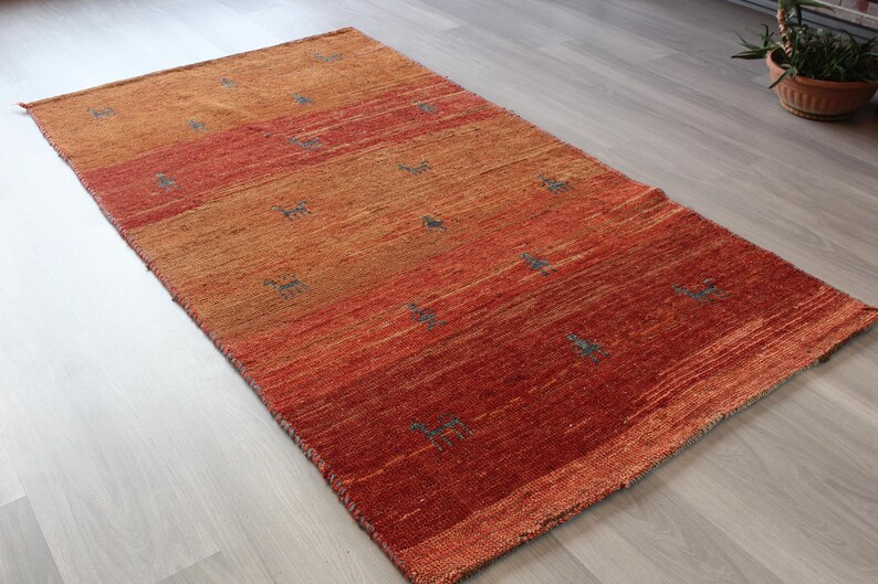 May include: A hand-woven rug with a gradient of orange, red, and brown hues. The rug features a subtle pattern of small, repeating shapes throughout.