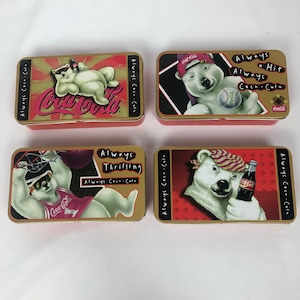 May include: Four vintage Coca-Cola collectible tins featuring a polar bear in different scenes. The tins are gold with red accents and feature the Coca-Cola logo. The text on the tins reads "Always Coca-Cola" and "Always a Hit", "Always Thrilling", and "Always Coca-Cola".