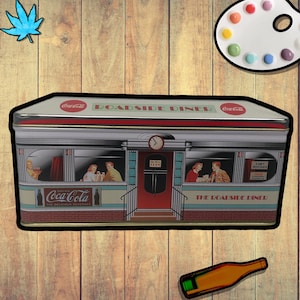 May include: A vintage-style metal tin box with a red, white, and blue design depicting a roadside diner. The tin box has the words "Coca-Cola" and "The Roadside Diner" printed on it.
