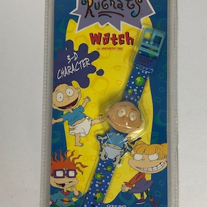 May include: A blue and yellow Rugrats watch with a 3-D character face. The watch features a blue band with white stars and green dots. The packaging includes a one-year limited warranty.