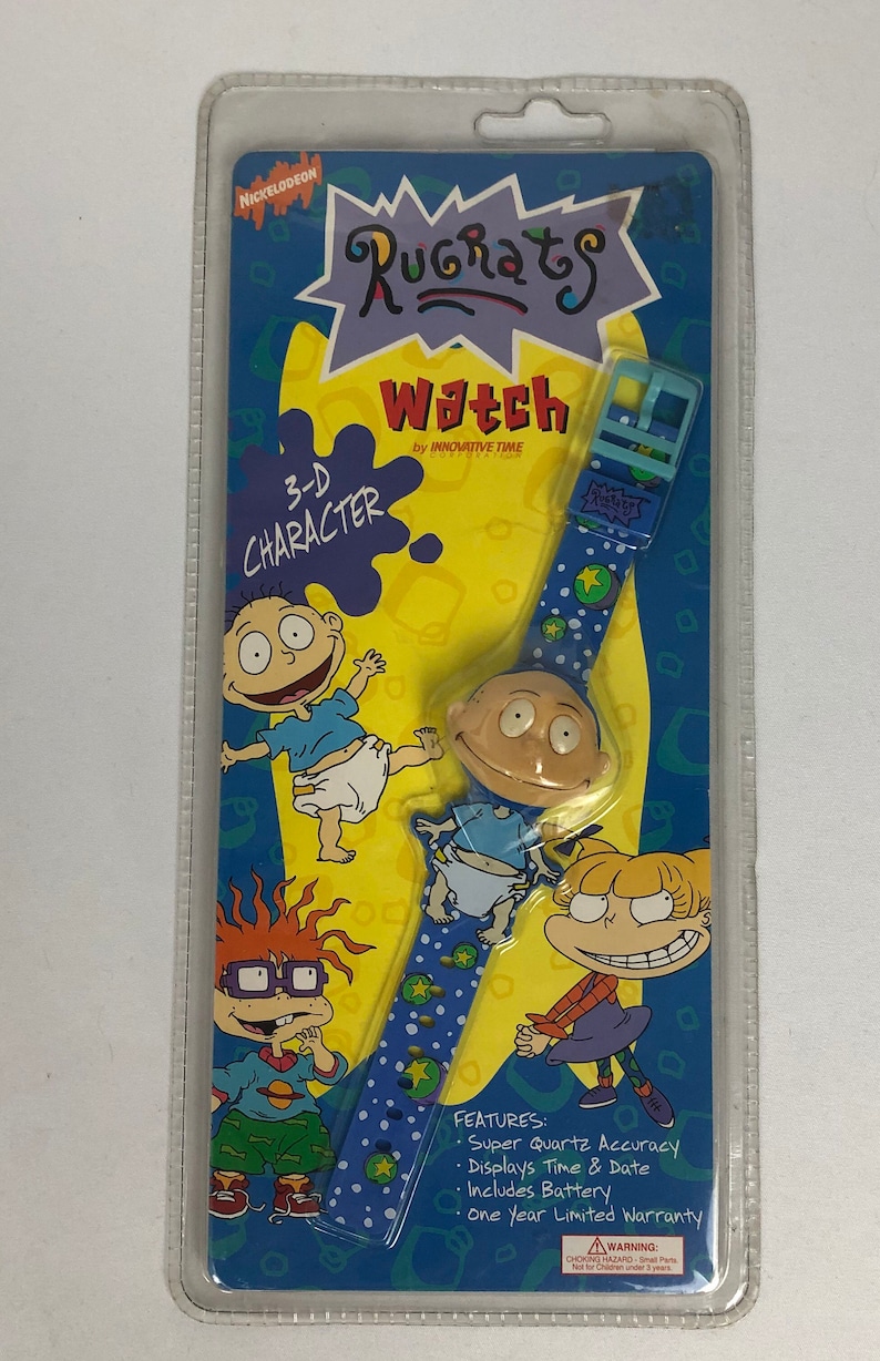 May include: A blue and yellow Rugrats watch with a 3-D character face. The watch features a blue band with white stars and green dots. The packaging includes a one-year limited warranty.