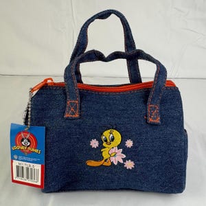 May include: A denim handbag with an embroidered Tweety Bird design and pink flowers. The bag has orange stitching and a matching zip. A Looney Tunes tag is attached.