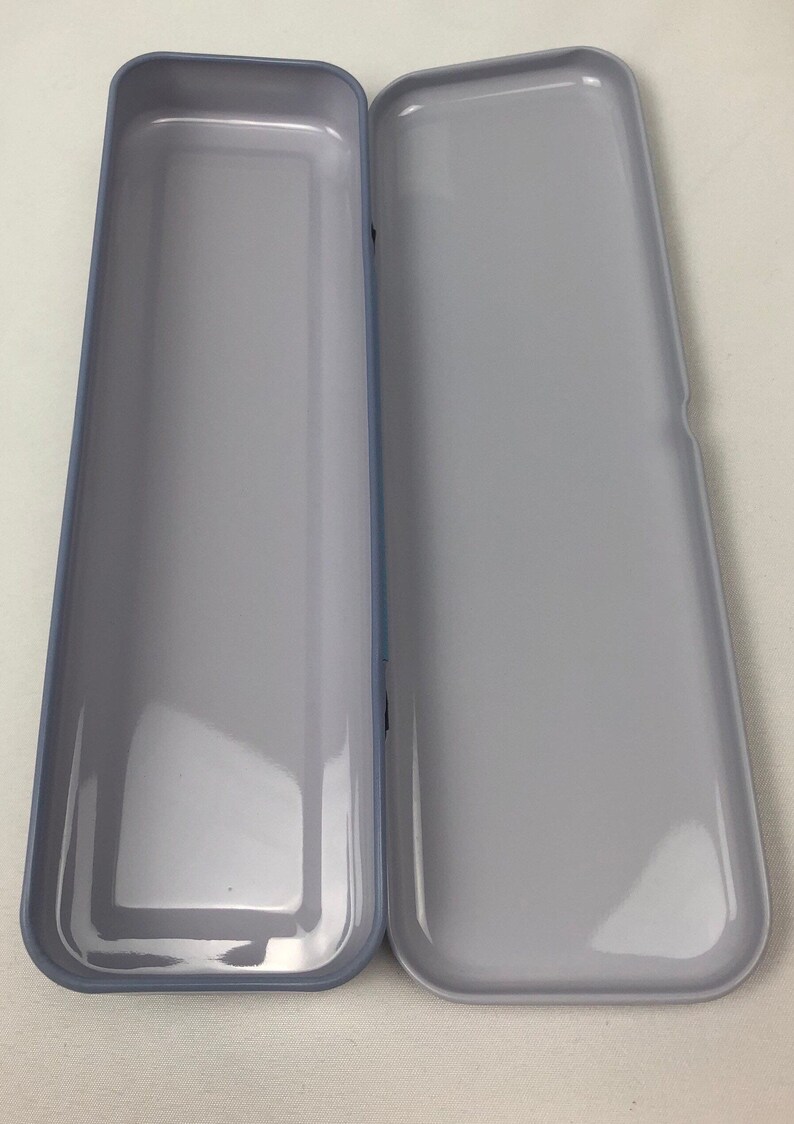 May include: A gray metal pencil case with a smooth, shiny finish. The case is open and empty.