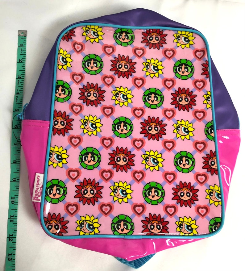 May include: A pink, purple, and blue backpack with a Powerpuff Girls design. The backpack features a repeating pattern of the Powerpuff Girls' faces in sunflowers with hearts on a pink background.