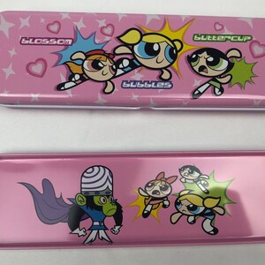 May include: Pink metal pencil case featuring the Powerpuff Girls, Blossom, Bubbles, and Buttercup. The case has a white interior and a separate compartment for storing pencils and other supplies. The case also features the Powerpuff Girls' arch-nemesis, Mojo Jojo.