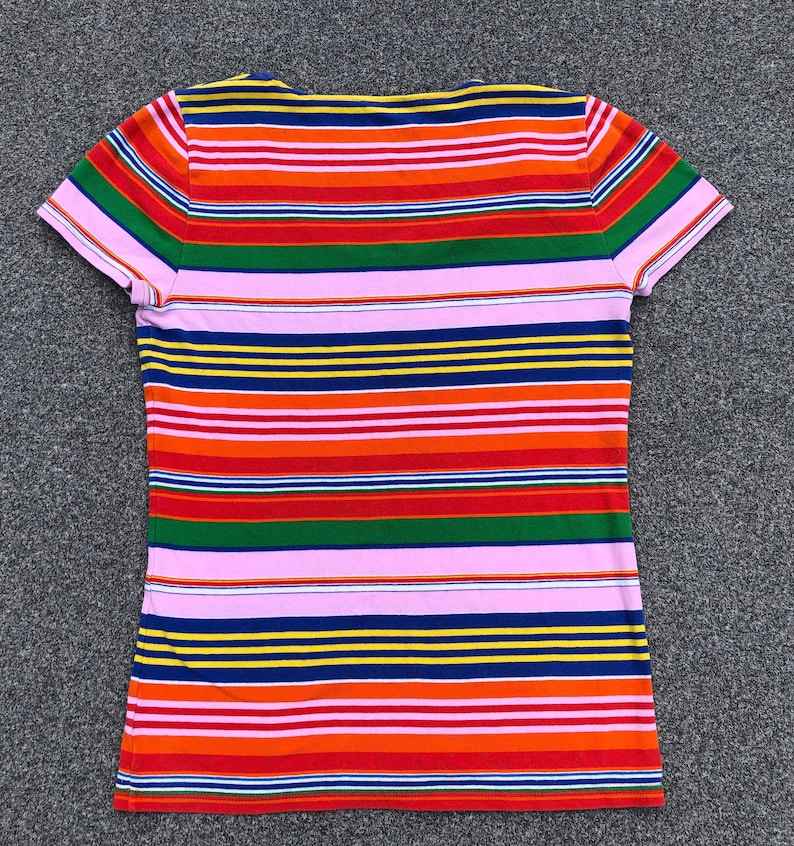 Peut inclure: Un t-shirt &agrave; manches courtes ray&eacute; avec un col en V. Le t-shirt a des rayures altern&eacute;es de rose, rouge, orange, jaune, vert, bleu et marine.