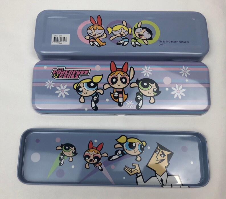 May include: A blue metal pencil case with a design featuring the Powerpuff Girls characters. The case has a striped pattern with white flowers and the words "The Powerpuff Girls" in a white box. The case is closed and the top of the case has a design of the Powerpuff Girls characters with the text "TM & &copy; Cartoon Network (s01)".