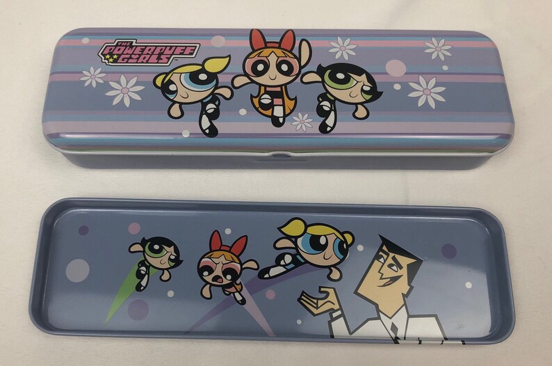 May include: A purple and blue metal pencil case with a graphic of the Powerpuff Girls. The case is closed and the top has the words "The Powerpuff Girls" printed on it. The bottom of the case has a graphic of the Powerpuff Girls and Professor Utonium.