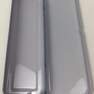 May include: A light gray metal pencil case with a slightly rounded rectangular shape. The case is open and empty.