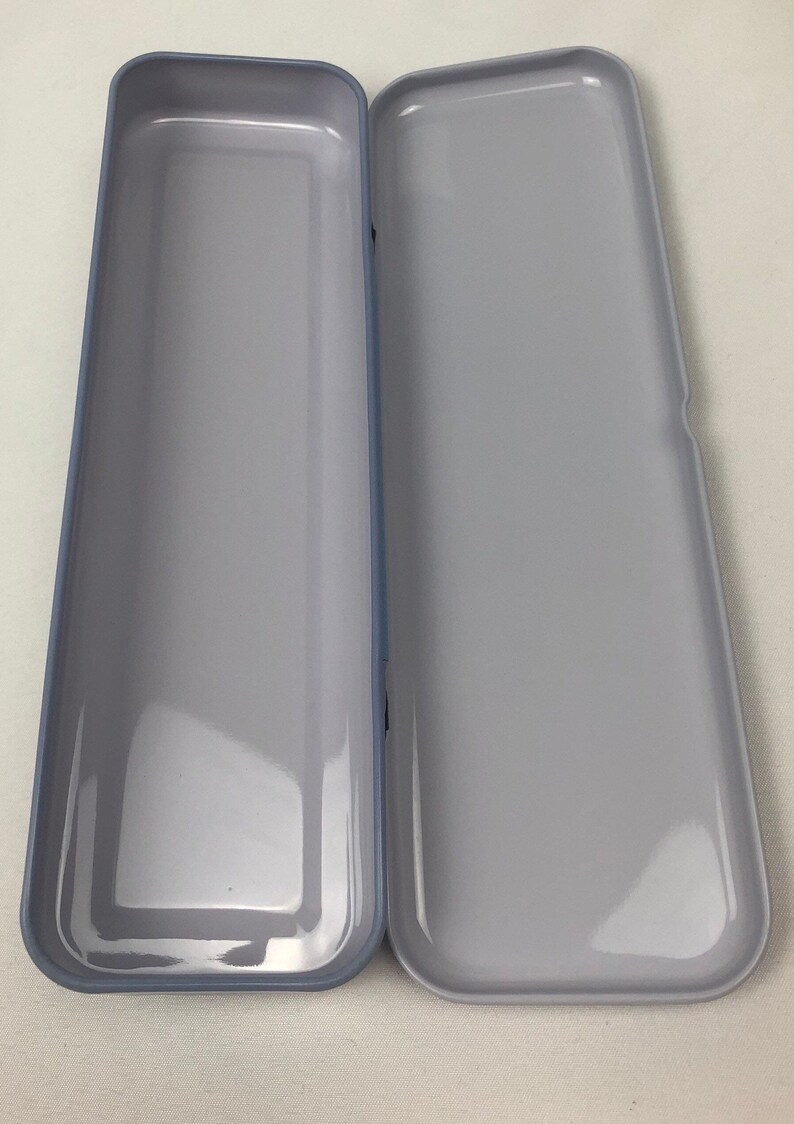 May include: A light gray metal pencil case with a slightly rounded rectangular shape. The case is open and empty.