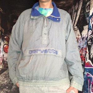 May include: A light blue windbreaker jacket with a blue collar and a zip closure. The jacket has a large "corvette" logo on the front.