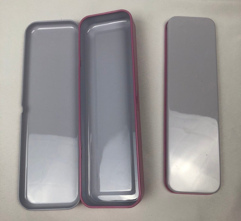 May include: Three empty rectangular tin boxes with a pink trim. The boxes are open and have a silver interior.