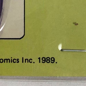 K&ouml;nnte beinhalten: Ein lila-wei&szlig;es Spielzeugtelefon aus Plastik mit gelbem Hintergrund. Das Telefon hat ein schwarzes Zifferblatt und ein schwarzes Kabel. Die Verpackung enth&auml;lt den Text "TM & &copy; DC Comics Inc. 1989." und "QUINTEL".