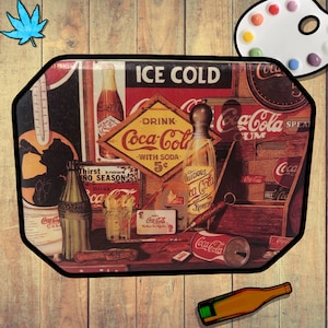May include: A vintage metal Coca-Cola tray with a red, white, and yellow color scheme. The tray features a variety of Coca-Cola imagery, including bottles, cans, and signs. The text "ICE COLD" and "DRINK Coca-Cola WITH SODA 5¢" is visible on the tray.