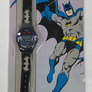 K&ouml;nnte beinhalten: Eine schwarz-gelbe Batman LCD-Digitaluhr mit im Dunkeln leuchtenden Emblemen. Die Uhr ist in einer Plastik-Blisterverpackung mit einem Comicbild von Batman verpackt. Die Verpackung enth&auml;lt auch den Text "BATMAN TM LCD DIGITAL WATCH BAT EMBLEMS GLOW IN THE DARK! QUINTEL TM&DC Comics Inc. 1989".