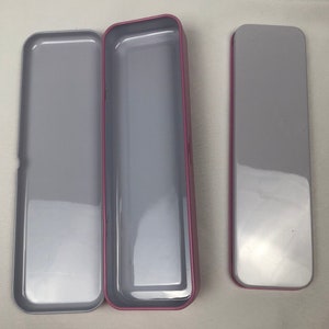 May include: Three empty rectangular tin boxes with a pink trim. The boxes are open and have a silver interior.