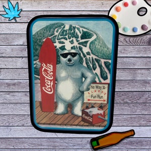 May include: A vintage Coca-Cola advertisement featuring a polar bear wearing sunglasses and holding a red surfboard with the Coca-Cola logo. The bear is standing on a wooden platform in front of a snowy mountain scene with the text "This Way to Always Fun Run".