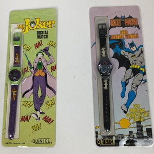 K&ouml;nnte beinhalten: Zwei Uhrenverpackungen mit dem Joker und Batman. Die Joker-Uhr hat ein violettes Armband mit einem gr&uuml;nen Zifferblatt und dem Text "The Joker" und "Digital Watch". Die Batman-Uhr hat ein schwarzes Armband mit einem schwarzen Zifferblatt und dem Text "Bat Man" und "LCD Digital Watch".