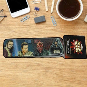 Puede incluir: Una caja de lápices de Star Wars Episodio I con Darth Maul, Qui-Gon Jinn y Obi-Wan Kenobi. La caja es negra con un borde plateado y tiene las palabras "Star Wars Episodio I" y "Pencil Box" impresas en ella.