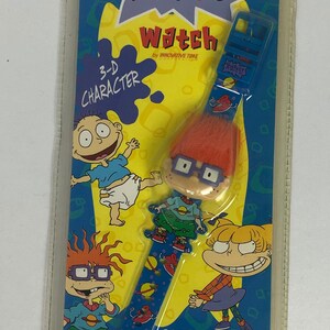 May include: A blue and yellow plastic package with a Nickelodeon Rugrats watch featuring a 3-D character. The watch has a blue band with a space-themed design and a 3-D character of Chuckie Finster with orange hair and glasses. The package features the text "Rugrats Watch" and "3-D Character".