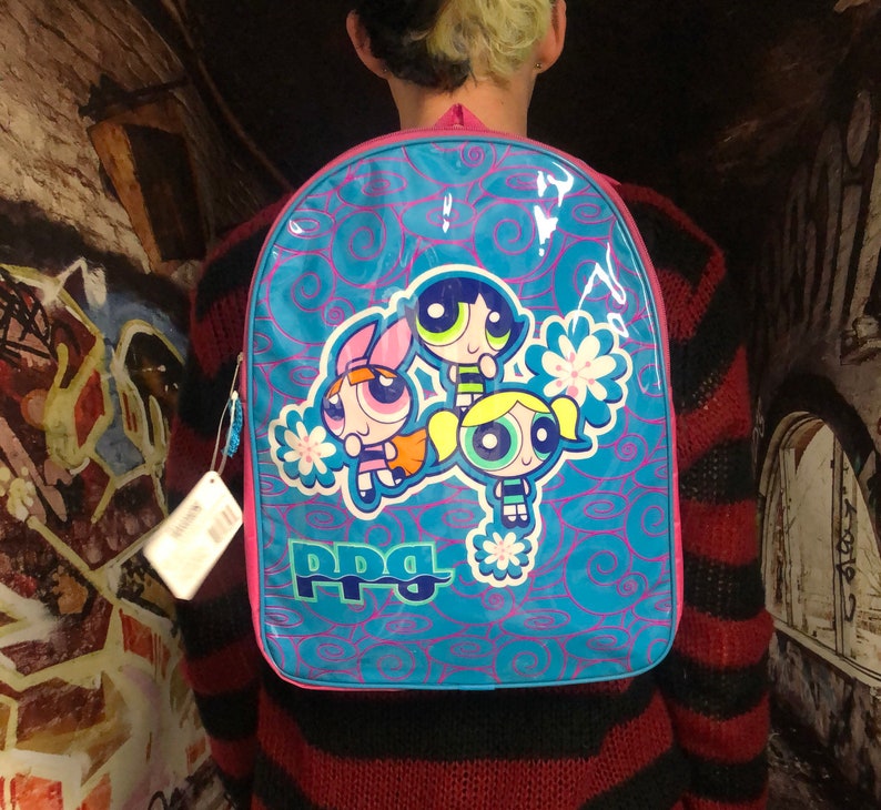 May include: A blue and pink backpack with a swirling pattern. The front of the backpack features a graphic of the Powerpuff Girls, with the text "ppg" below them.