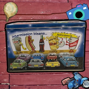 May include: A blue and white metal tin with a Coca-Cola theme. The tin features a cartoon illustration of a hot dog, popcorn, and a Coca-Cola bottle. The text on the tin reads "Intermission Means... Refreshment".