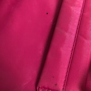 May include: A close-up of a pink fabric backpack with visible stitching and two small black marks.