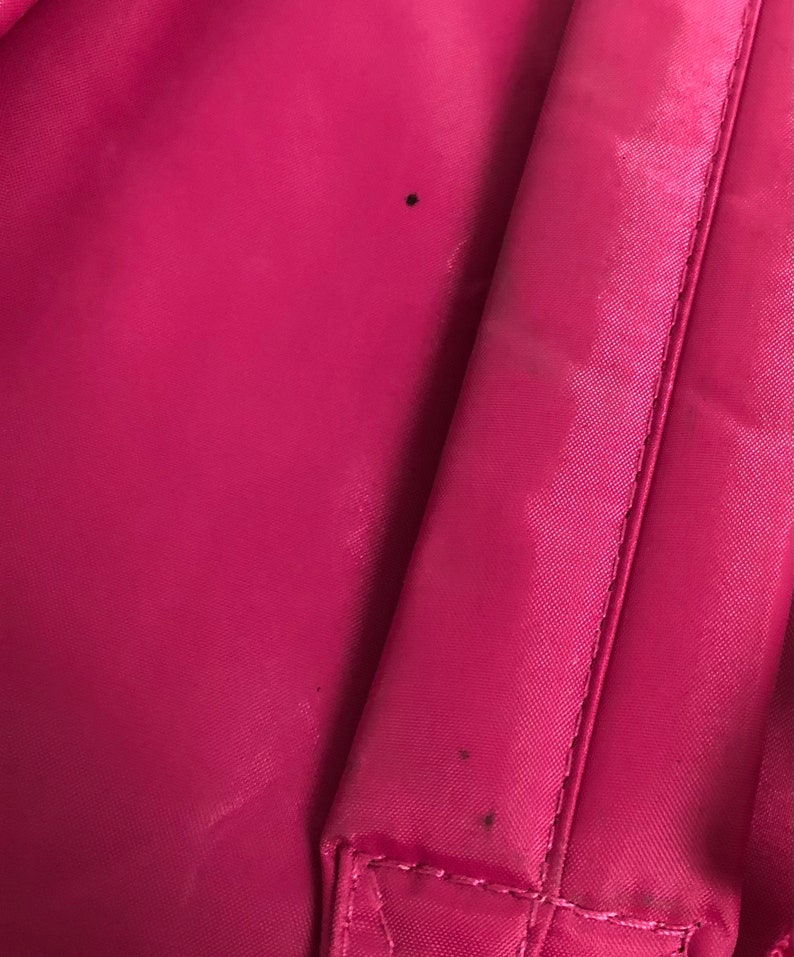 May include: A close-up of a pink fabric backpack with visible stitching and two small black marks.