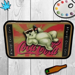 May include: A vintage Coca-Cola tin with a polar bear wearing sunglasses and holding a bottle of Coca-Cola. The tin has a red, white, and gold design with the words "Always Coca-Cola" on the side.