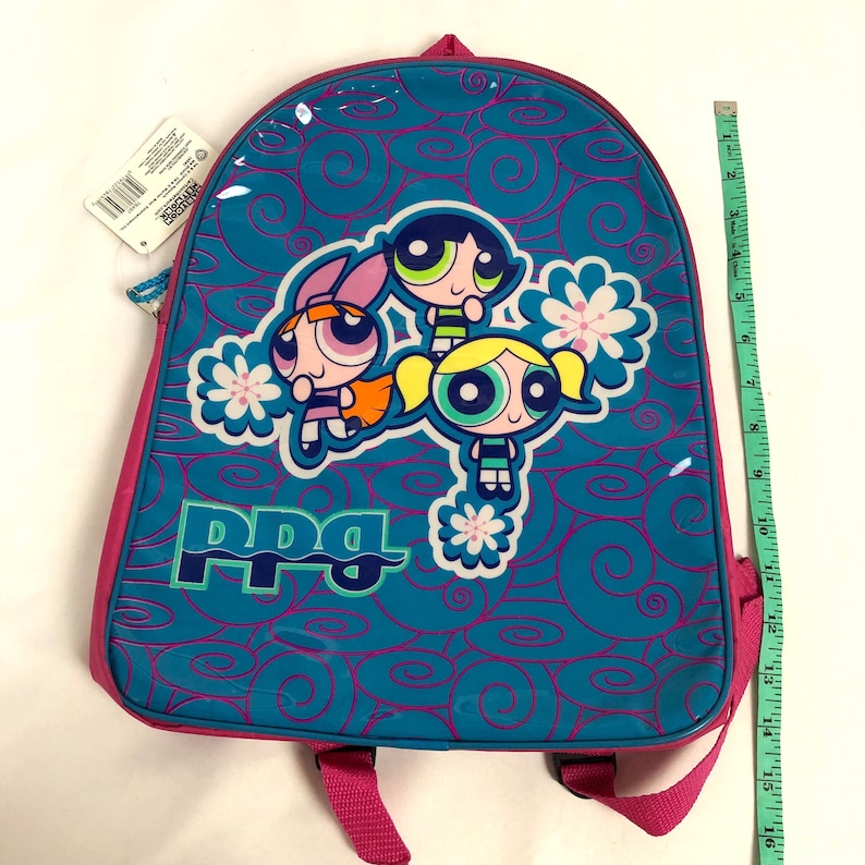 May include: A blue and pink backpack with a Powerpuff Girls design. The backpack features the three girls, Blossom, Bubbles, and Buttercup, with the words "PPG" printed on the front.