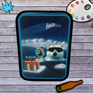 Puede incluir: Una lata vintage de Coca-Cola con un oso polar que lleva gafas de sol y sostiene una botella de Coca-Cola. El oso está de pie en un paisaje nevado con un paquete de seis Coca-Cola en el fondo. La lata tiene un fondo azul con estrellas y un cometa.