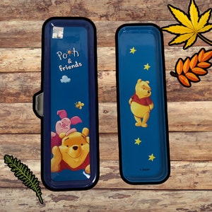 May include: A blue pencil case with a Winnie the Pooh and friends design. The case has a zipper closure and features a yellow Winnie the Pooh character with Piglet on his back. The other side of the case has a single yellow Winnie the Pooh character with stars and the text "© DISNEY".