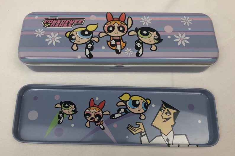 May include: A purple and blue metal pencil case with a graphic of the Powerpuff Girls. The case is closed and the top has the words "The Powerpuff Girls" in white. The bottom of the case has a graphic of the Powerpuff Girls and Professor Utonium.