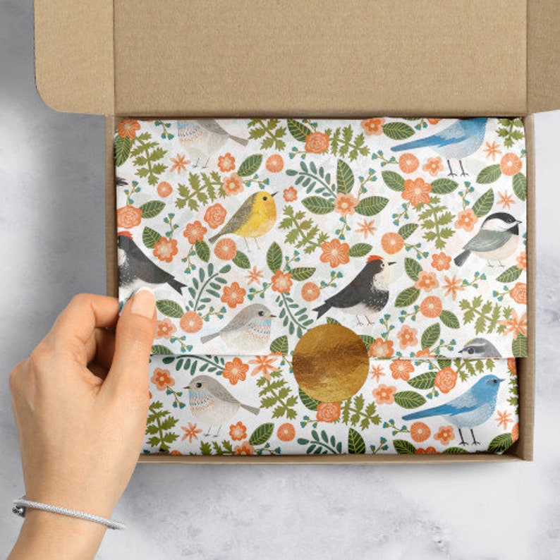 May include: A sheet of white tissue paper with a repeating pattern of colorful birds and flowers. The birds are blue, yellow, black, and gray. The flowers are orange and white.