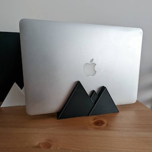 May include: A black laptop stand shaped like a mountain range. The stand is made of plastic and has a matte finish. The stand is designed to elevate a laptop for better ergonomics.