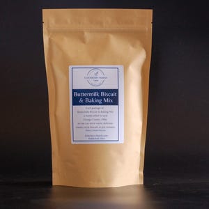 May include: A brown paper bag of Buttermilk Biscuit & Baking Mix. The label is white with blue text and includes the text "ELDERBERRY MARSH FARM" at the top. The label also states that the mix is handcrafted in rural Geauga County, Ohio.