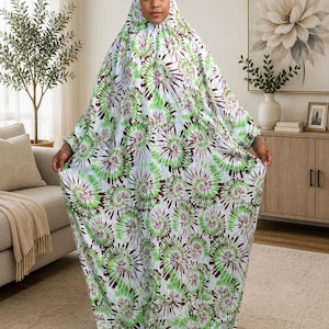 May include: A full-length, loose-fitting garment featuring a white base with a repeating tie-dye pattern in shades of green and dark brown. The piece includes an integrated hood that covers the head and flows down into a wide, floor-length silhouette.