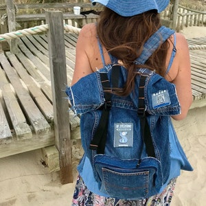 Op de afbeelding: Een denim bucket hat en rugzak set. De hoed en rugzak zijn gemaakt van verschillende tinten blauwe denim. De rugzak heeft zwarte bandjes en een voorvak. De rugzak heeft een patch met de tekst "UP CYCLOTHING".